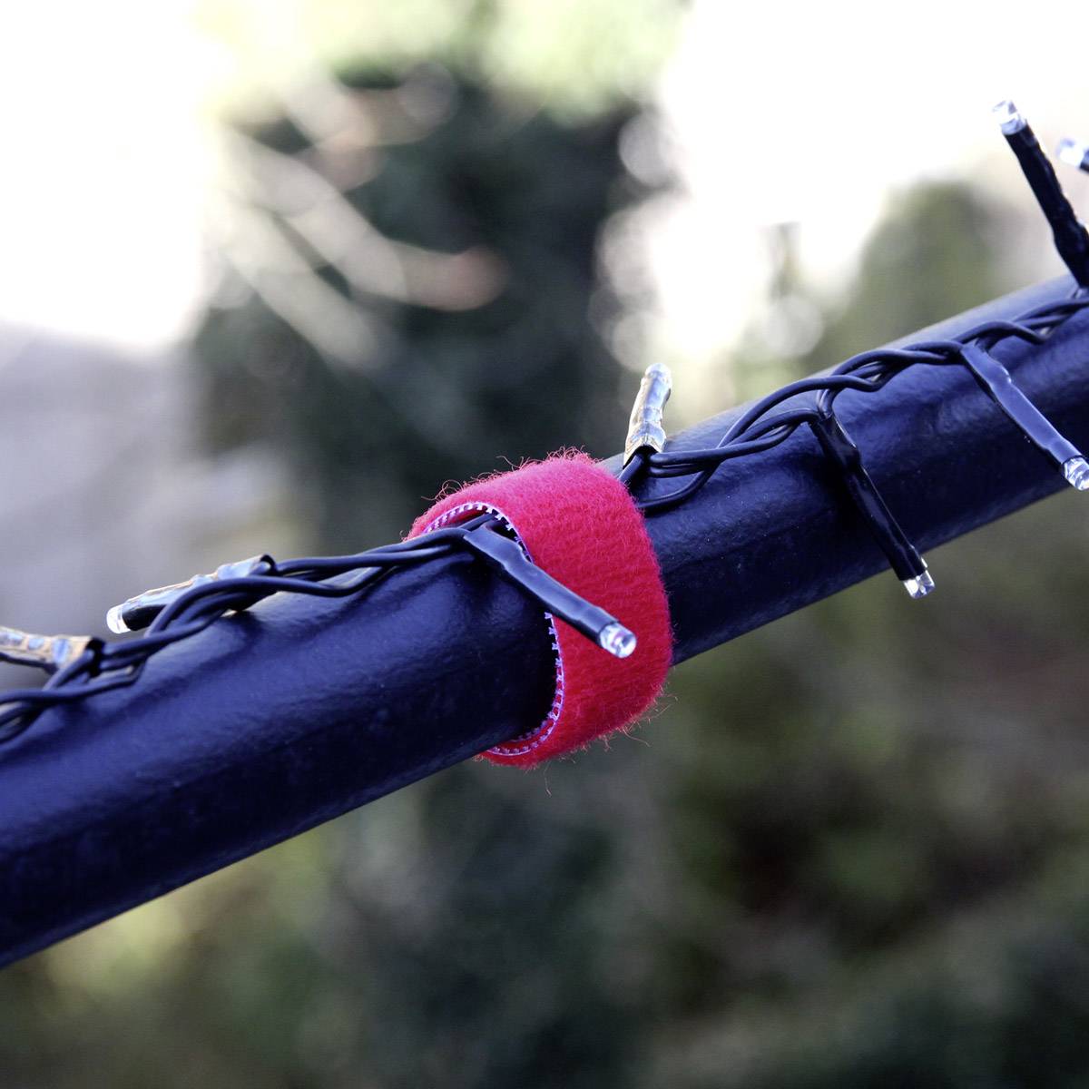 Ein schwarzes Kabel, umwickelt mit einer roten Klettband-Schlaufe, vor unscharfem Hintergrund.