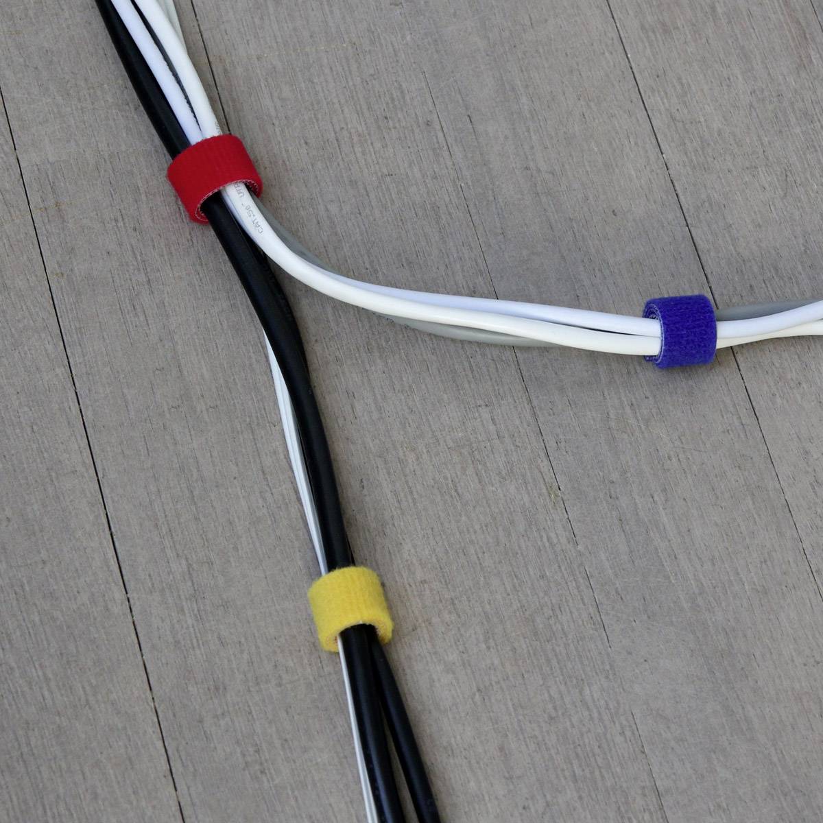 Mehrere Kabel sind parallel verlegt und mit Kabelbindern in den Farben Rot, Gelb und Blau auf einem Holzuntergrund fixiert.