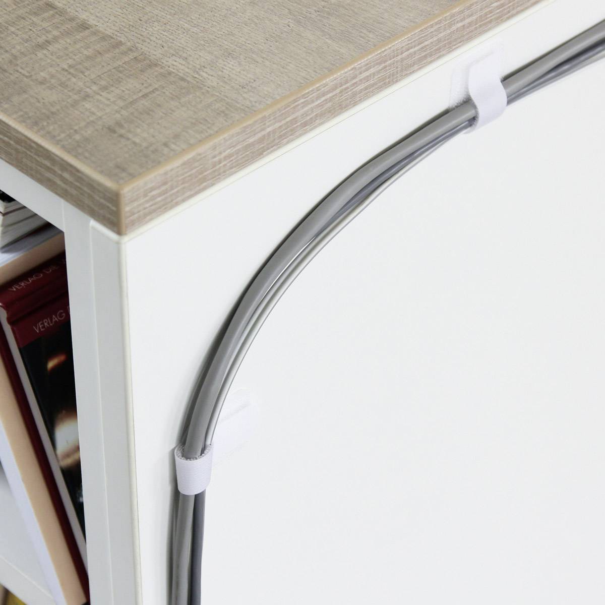 Ein Regal mit Holzoberfläche, Kabel werden seitlich mit Kabelhaltern ordentlich befestigt. Daneben sind Bücher zu sehen.