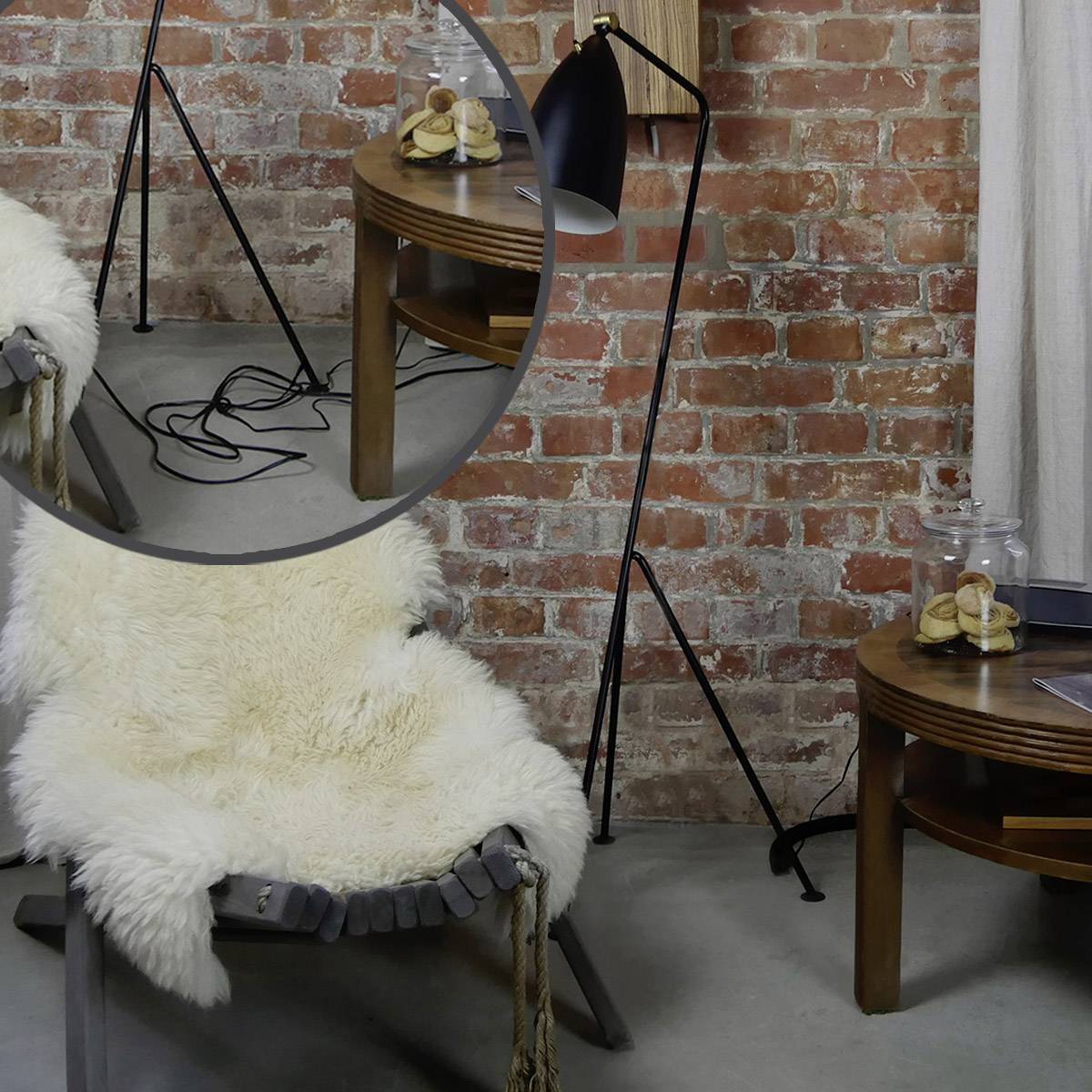Ein gemütlicher Raum mit Ziegelwand, Fellstuhl und runder Spiegel. Kabel, Tischlampen und runder Tisch mit Büchern und Getränken.