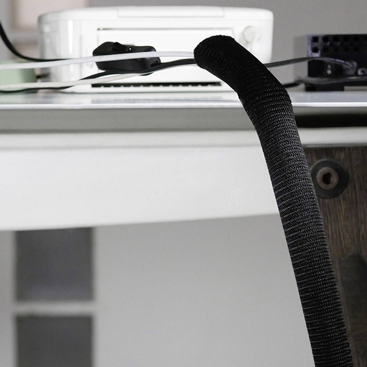 Ein schwarz ummanteltes Kabel hängt über einer Tischkante.