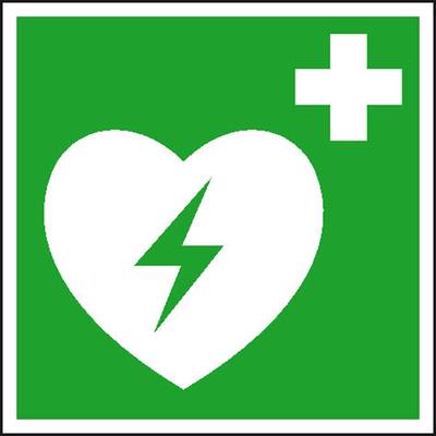 Ein grünes Schild mit einem weißen Herz und einem Blitzsymbol, das auf einen Defibrillator hinweist, plus Zeichen oben rechts.