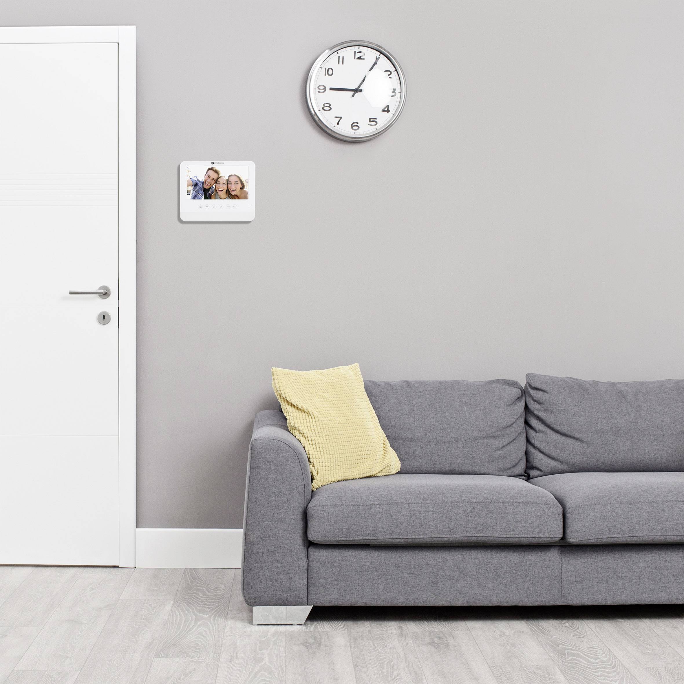 Graues Wohnzimmer mit einem Sofa, darüber eine Wanduhr und ein digitales Bilderrahmenfoto mit lächelnden Personen.