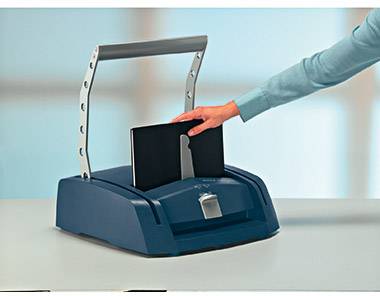 Eine Person legt ein Dokument in ein blaues Bindegerät auf einem Tisch ein, um es zu binden.
