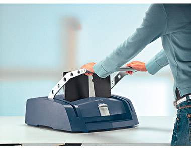 Eine Person benutzt eine Bindemaschine auf einem Tisch. Die Maschine hat einen blauen Korpus und der Benutzer hält ein Dokument.