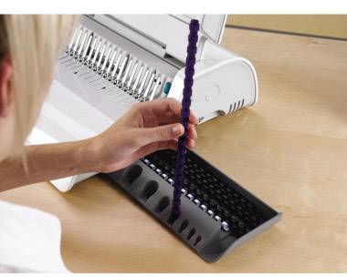 Eine Person bindet Dokumente mit einem Bindegerät auf einem Tisch. Sie hält einen violetten Plastikbinderstab in der Hand.