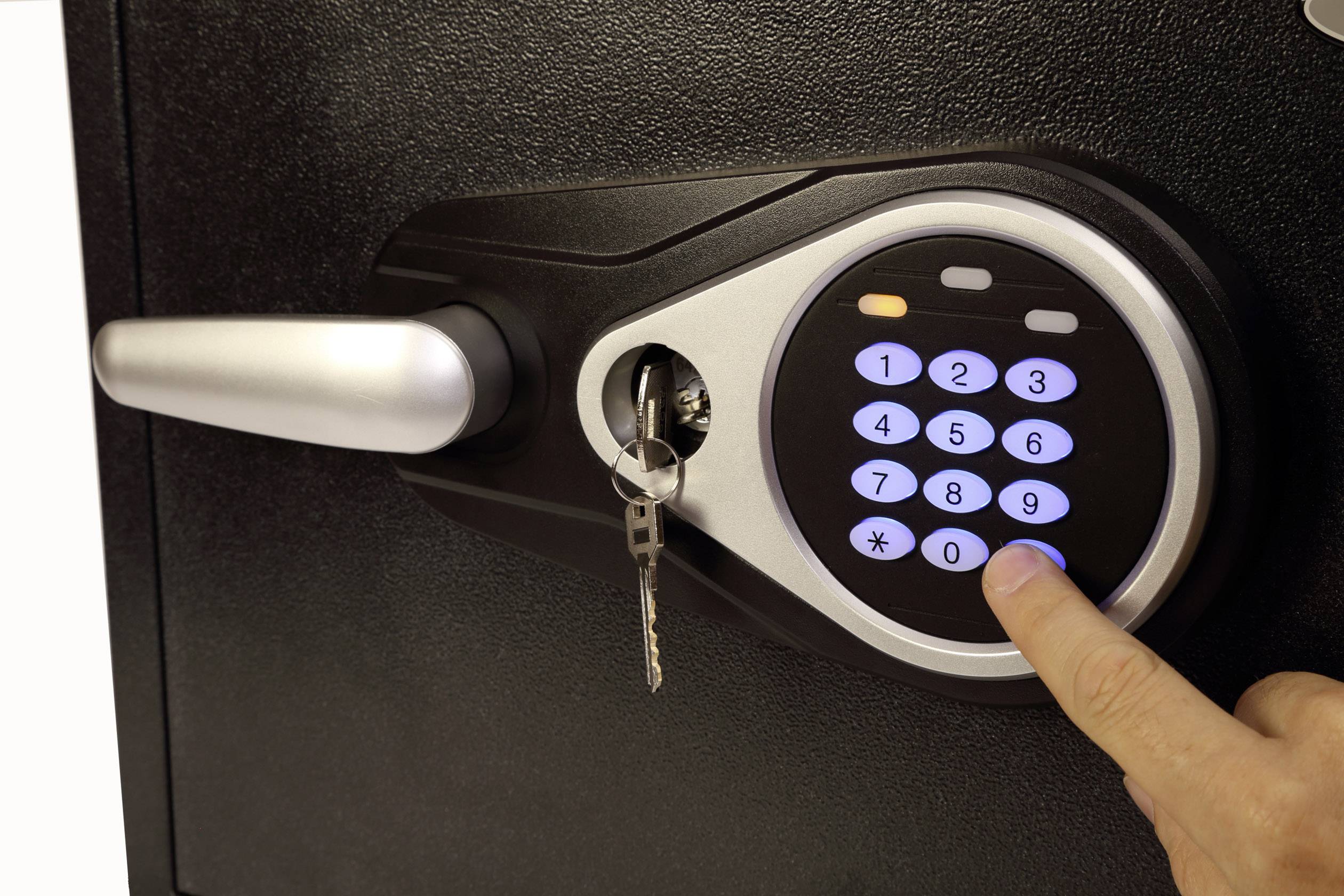 Eine Hand tippt eine Zahl auf einem elektronischen Tresorschloss. Ein Schlüssel steckt im Schloss neben dem Zahlenfeld.