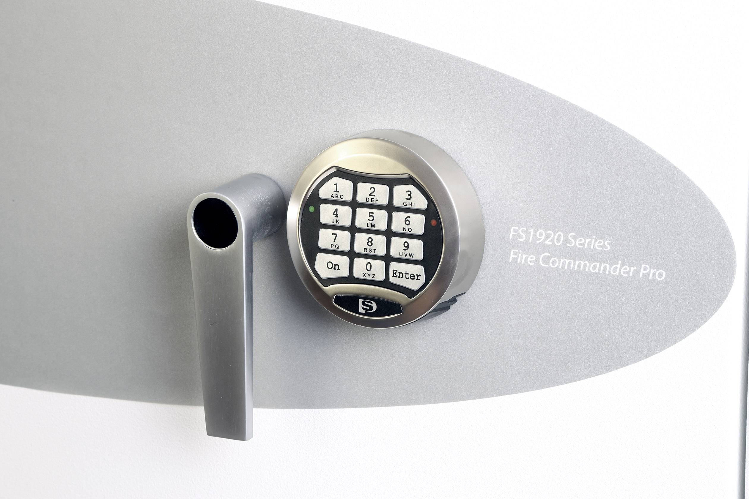 Ein elektronisches Zahlenschloss mit einem Drehgriff, daneben steht 'FS1920 Series Fire Commander Pro'.