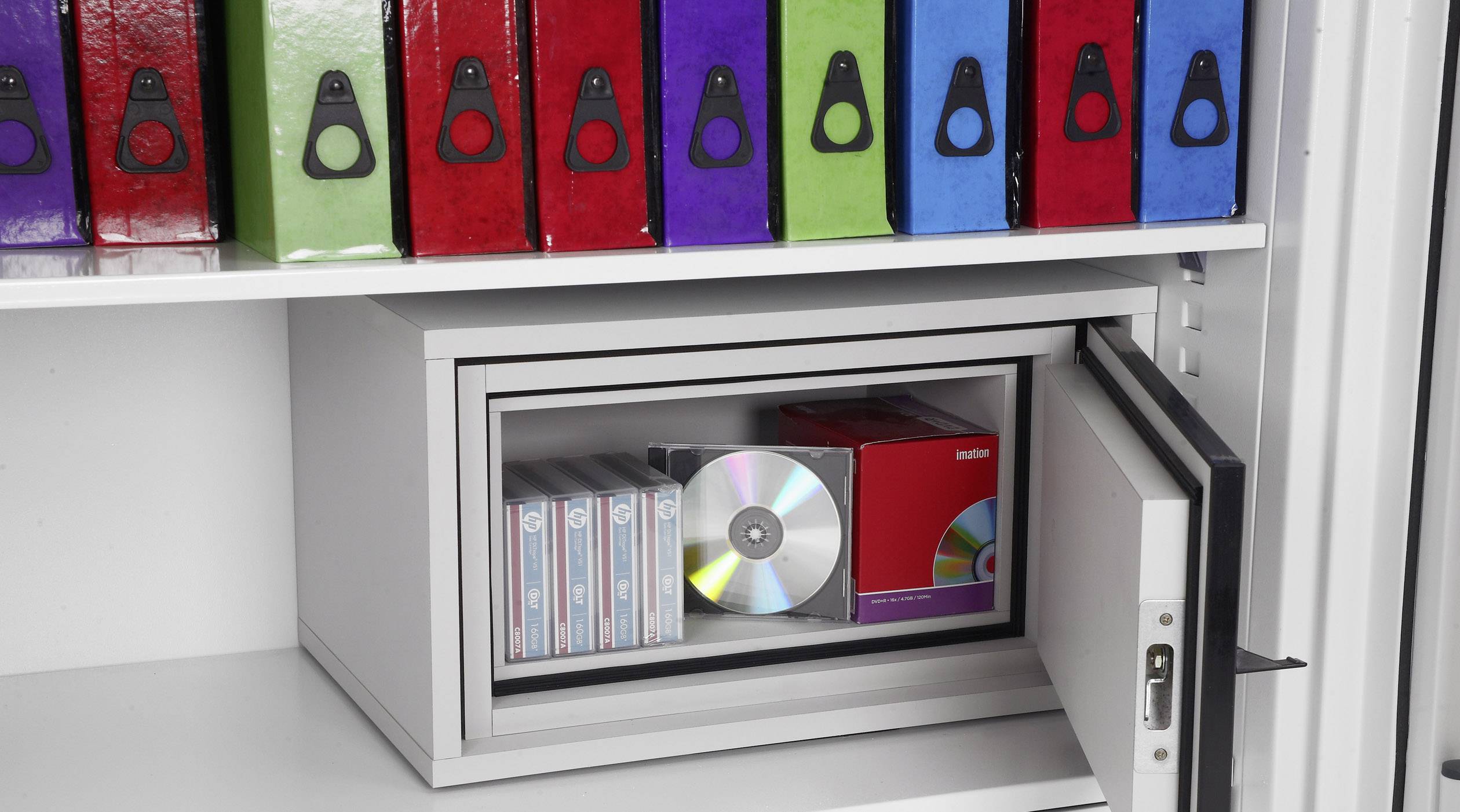 Ein sicherer Tresor enthält CDs, Kassetten und eine Festplatte; darüber sind farbige Aktenordner aufgereiht.