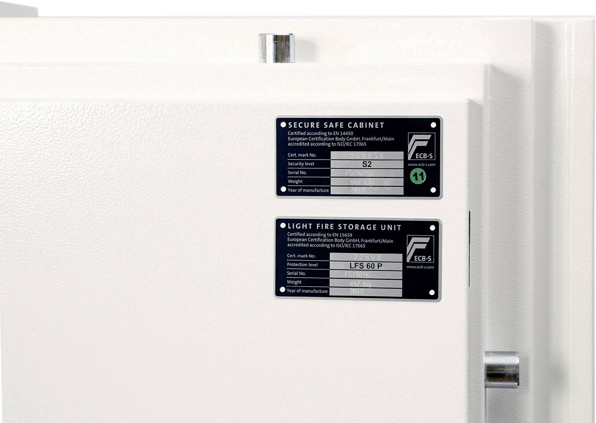 Ein weißer Safe mit zwei Etiketten: oben 'Secure Safe Cabinet', darunter 'Light Fire Storage Unit'. Beide Etiketten enthalten technische Details.