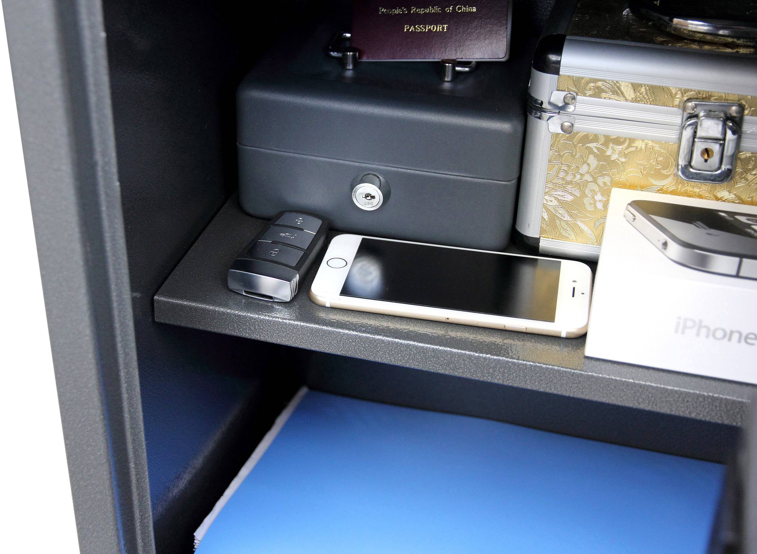Ein offener Safe mit einem Smartphone, einem Schlüsselfernbedienung, einer schwarzen Box mit Schloss, einem Reisepass und einem goldenen Koffer.