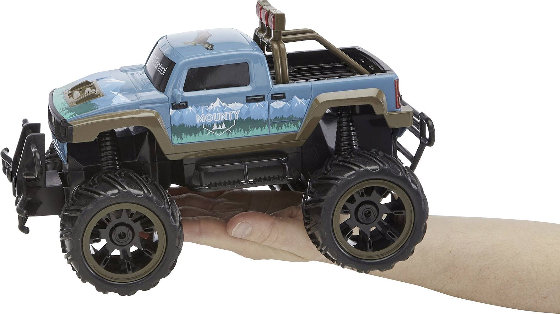 Eine Hand hält ein kleines, blaues Spielzeugauto im Geländewagenstil. Das Auto hat auffällige große Reifen und ein Bergmotiv.