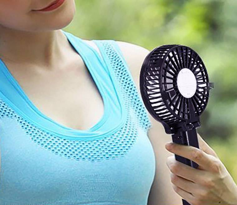 Eine Person hält einen kleinen tragbaren Ventilator, der an heißen Tagen zur Abkühlung dient.