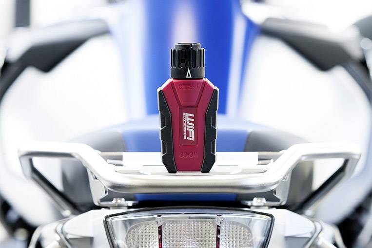 Ein roter Wiha-Schraubendreher mit schwarzem Griff liegt auf einem silbernen Regal. Im Hintergrund unscharf ein Motorradteil.