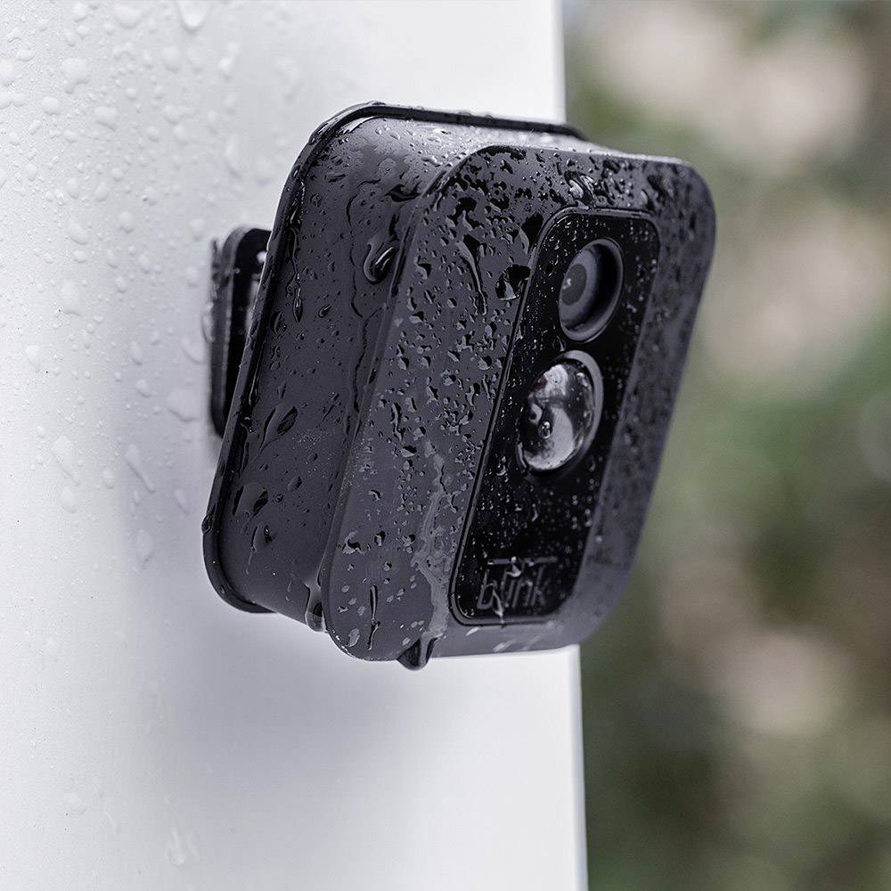 Eine schwarze, wetterfeste Überwachungskamera montiert an einer nassen Wand im Freien. Sie ist mit Wassertropfen bedeckt.