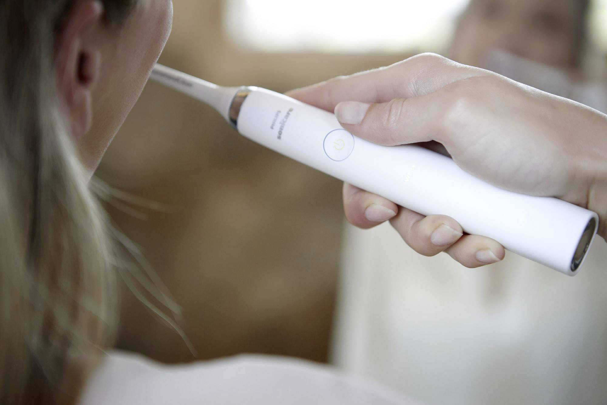 Eine Person hält eine elektrische Zahnbürste neben ihrem Gesicht, bereit zum Zähneputzen. Die Zahnbürste ist weiß und schlank.