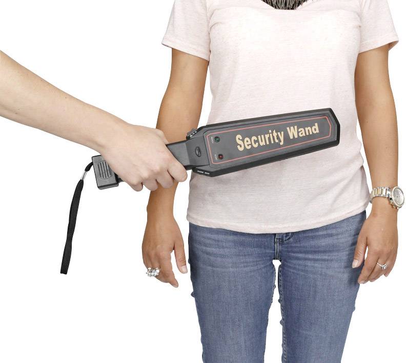 Eine Hand hält einen Sicherheitsstab und scannt eine stehende Person. Der Stab zeigt den Text 'Security Wand'.