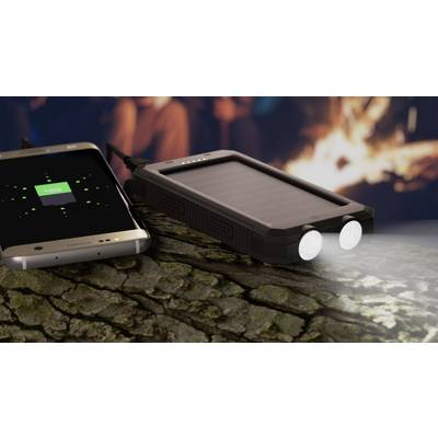 Ein Solar-Ladegerät lädt ein Smartphone, während es eine Taschenlampe betreibt. Hintergrund zeigt ein Lagerfeuer in unscharfer Ansicht.