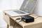 Ein Laptop mit Audiobearbeitungssoftware ist mit einem schwarzen Audio-Interface auf einem Holztisch verbunden.