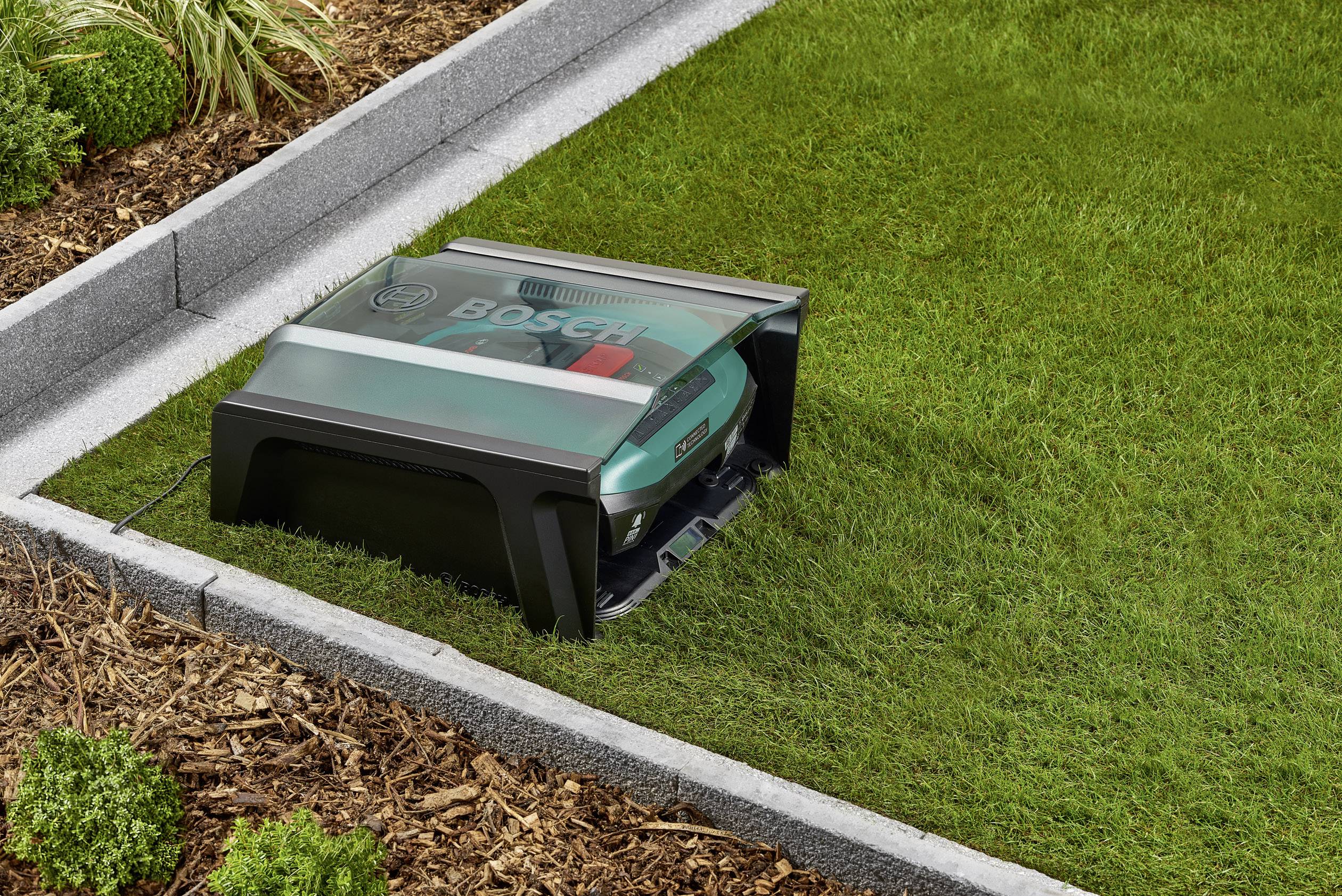 Ein Mähroboter mäht den Rasen in einem gepflegten Garten. Der Roboter befindet sich auf grasgrünem, rechteckigem Bereich, umgeben von Pflanzen.