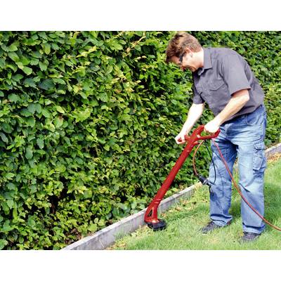 Eine Person trimmt mit einem Elektroschneider das Gras entlang einer Hecke in einem Garten.