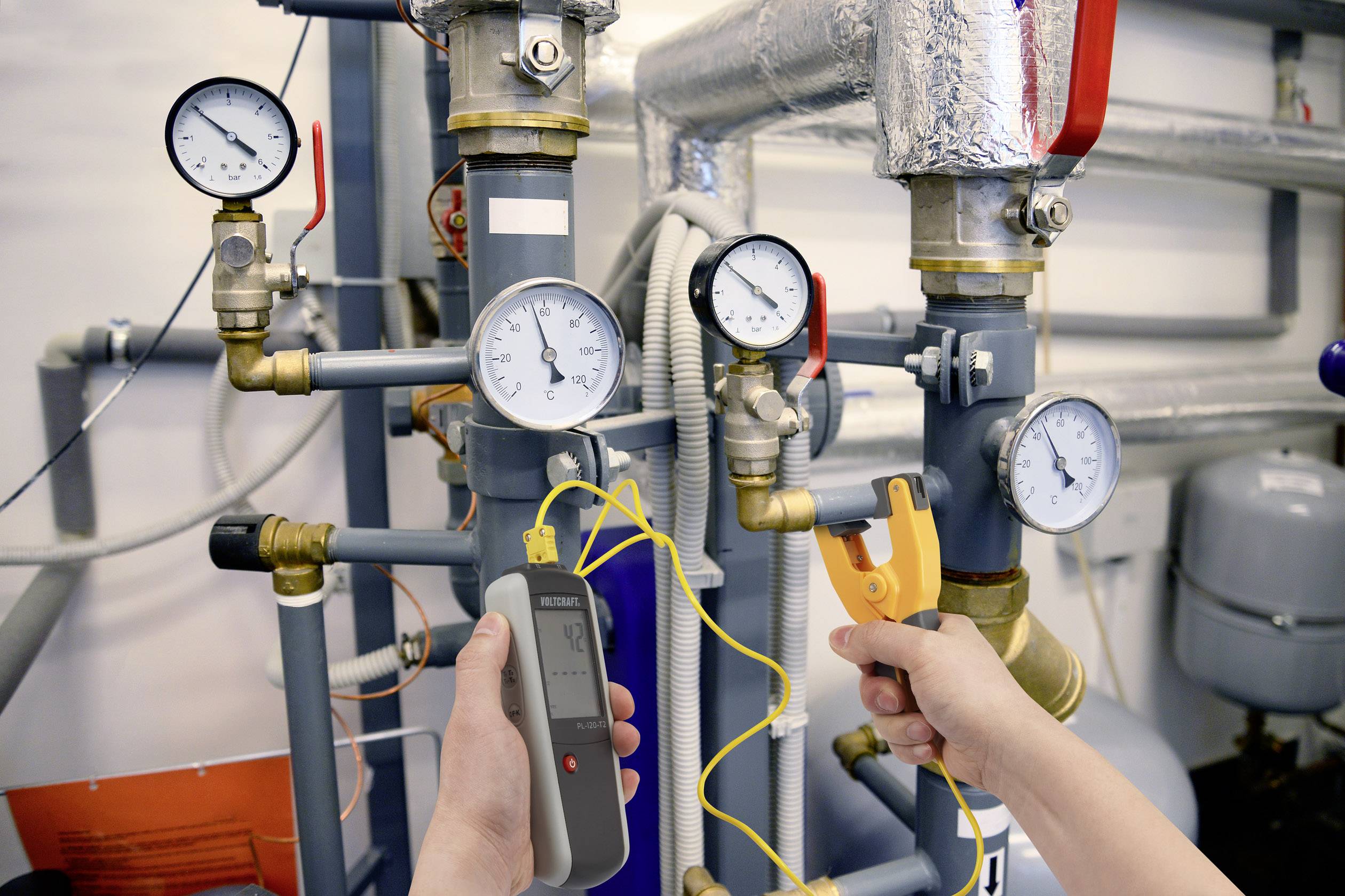 Ein Techniker misst mit einem digitalen Gerät den Druck in einem Rohrsystem. Manometer zeigen die Druckwerte an verschiedenen Punkten.