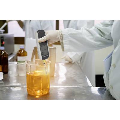 Eine Person in einem Labor misst mit einem Handmessgerät den pH-Wert einer orangefarbenen Flüssigkeit in einem Becherglas.