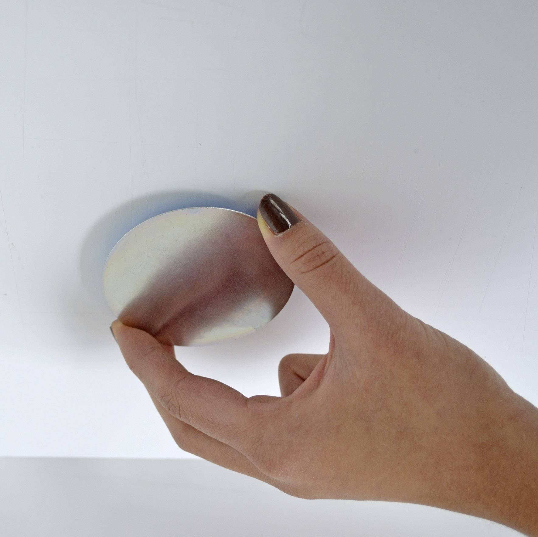Eine Hand legt einen runden metallischen Gegenstand an eine weiße Wand.