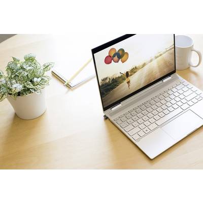 Silberner Laptop auf Holztisch mit Bild von Kind, das Luftballons hält. Daneben Kaffeetasse, Pflanze und Notizblock.