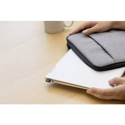Person legt einen geschlossenen Laptop in eine graue Hülle auf einem Holztisch. Im Hintergrund steht eine Tasse.