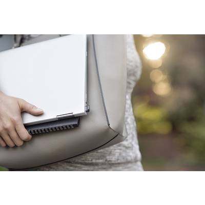 Eine Person trägt eine hellgraue Tasche mit einem Laptop und einem Notizbuch, im Freien bei Sonnenuntergang.