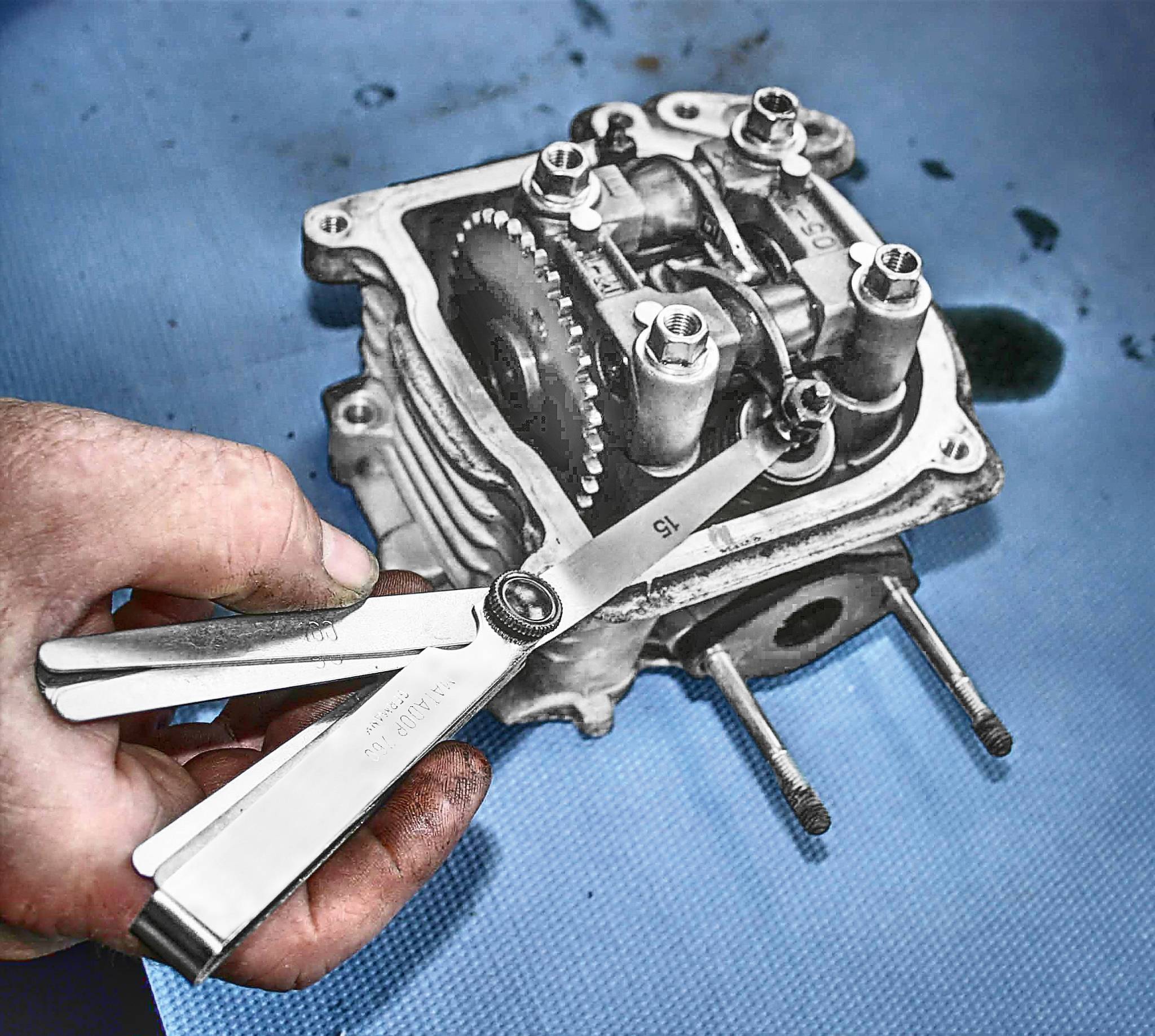 Eine Hand hält eine Fühlerlehre über einem Motorteil auf einem blauen Hintergrund, um Präzisionsmessungen durchzuführen.