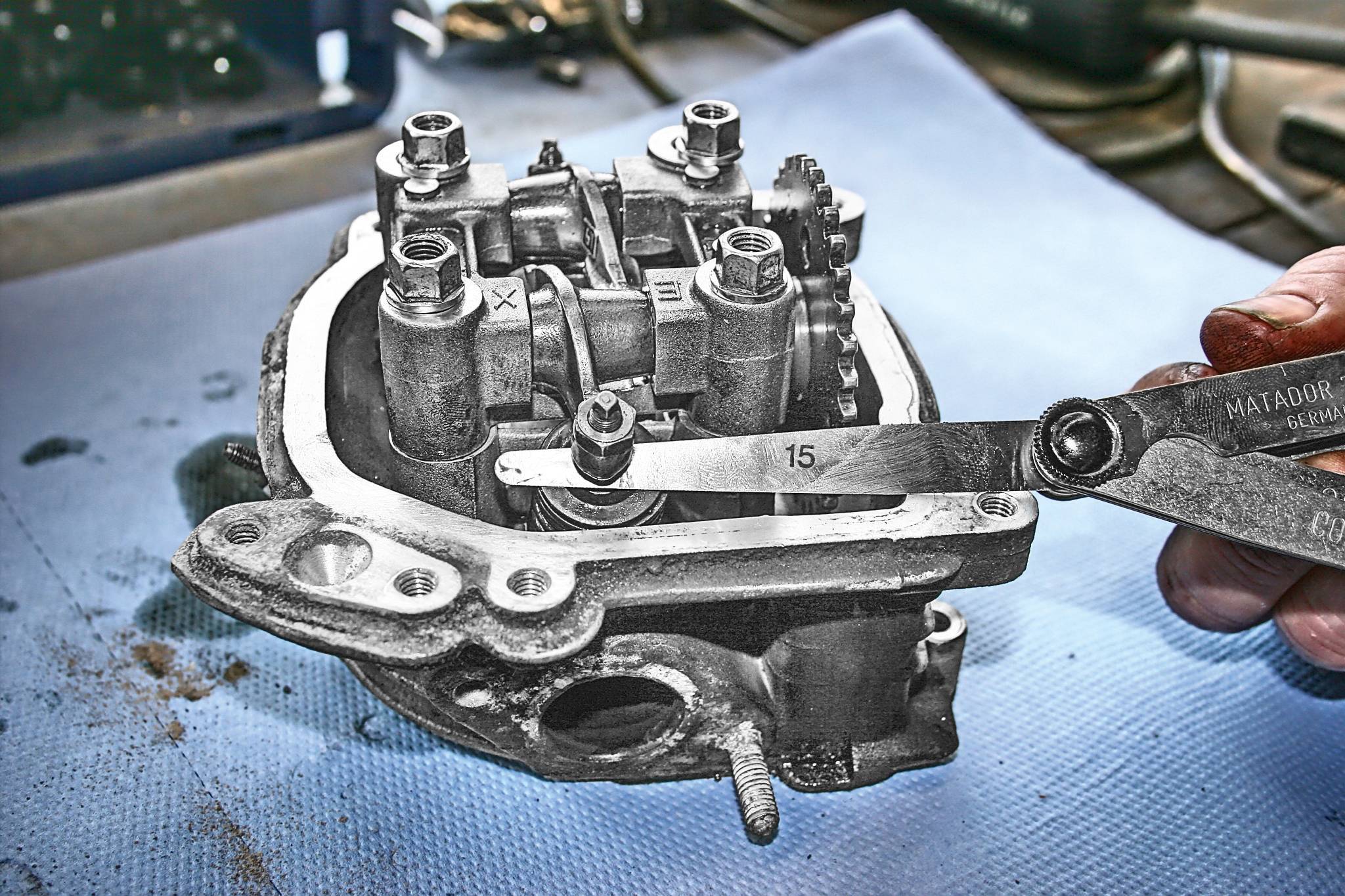 Mechaniker misst den Ventilabstand eines Motors mit einer Fühlerlehre. Der Motor liegt auf einem blauen Tuch in einer Werkstatt.