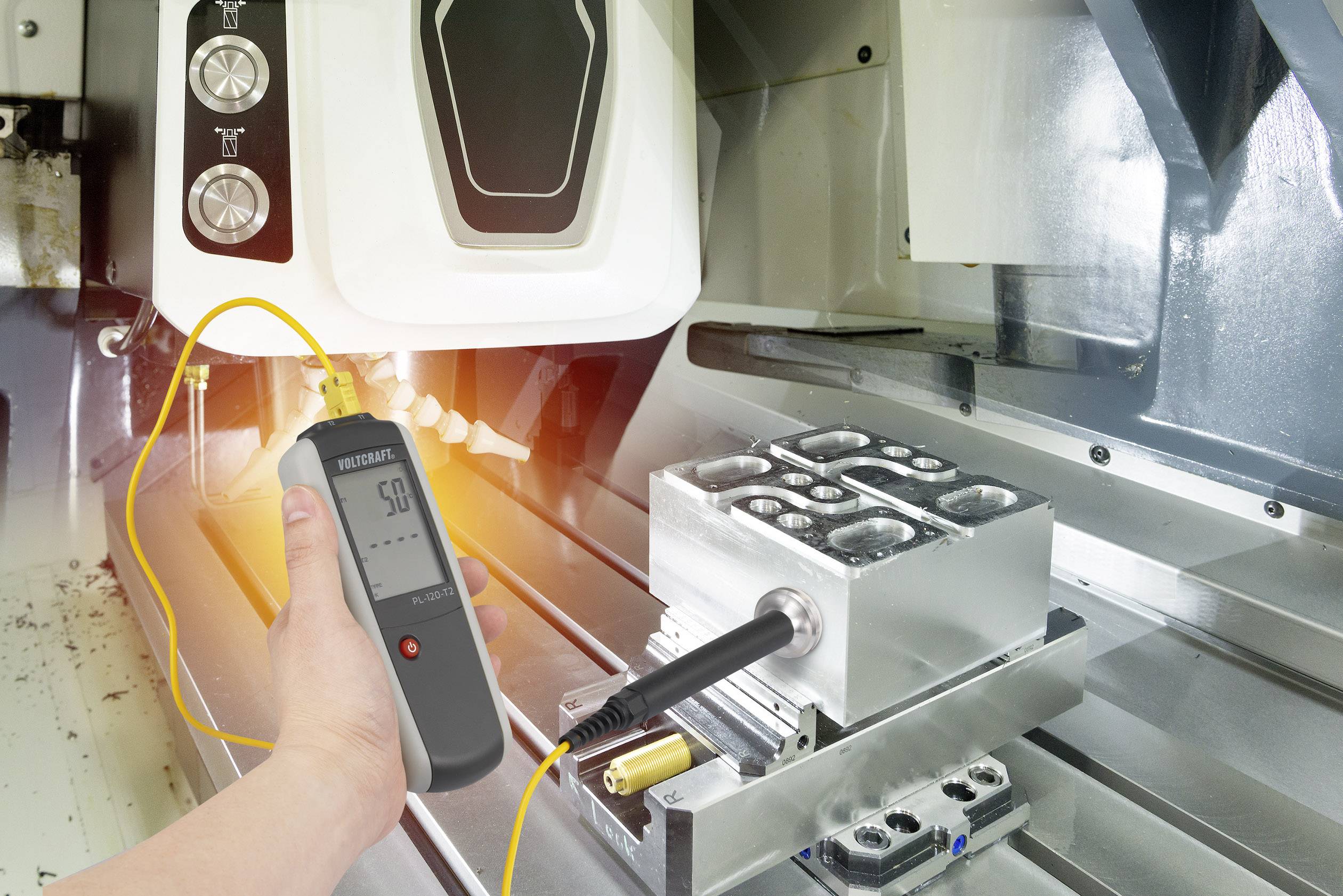 Eine Person misst die Temperatur eines Metallblocks mit einem digitalen Thermometer in einer Werkstattumgebung.