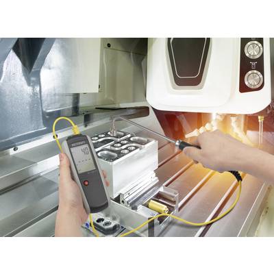 Eine Person misst die Temperatur eines Metallteils in einer industriellen Umgebung mit einem digitalen Thermometer.