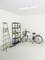 Ein heller Raum mit einem Fahrrad, einem Regal mit Reinigungsmitteln, einer Leiter und einem Besen; wirkt wie eine Garage oder Abstellraum.