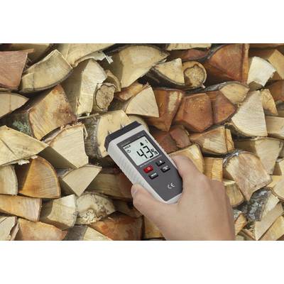 Eine Hand hält ein Feuchtigkeitsmesser an einen Stapel Holzscheite. Das Gerät zeigt '43,7%' an.