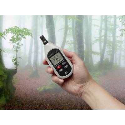 Eine Hand hält ein Hygrometer im Wald; Gerät zeigt 95,2 % Luftfeuchtigkeit und 26 °C Temperatur an, umgeben von nebligen Bäumen.