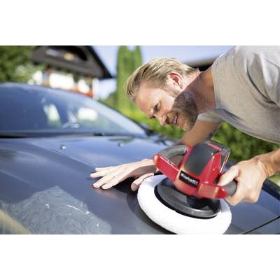 Mann poliert ein Auto mit einer elektrischen Poliermaschine im Freien, lächelt dabei und konzentriert sich auf die reflektierende Oberfläche.