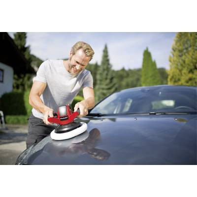 Ein Mann poliert die Motorhaube eines Autos mit einer Poliermaschine im Freien. Im Hintergrund sind Bäume und ein Gebäude zu sehen.