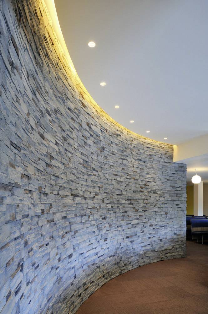 Geschwungene Wand aus Naturstein mit integrierter LED-Beleuchtung. Die warme Beleuchtung betont die Struktur und Farbe der Steine.