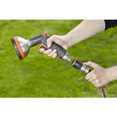Eine Person hält eine Gardena-Gartenspritze und befestigt einen Schlauch daran. Im Hintergrund ist eine Rasenfläche zu sehen.