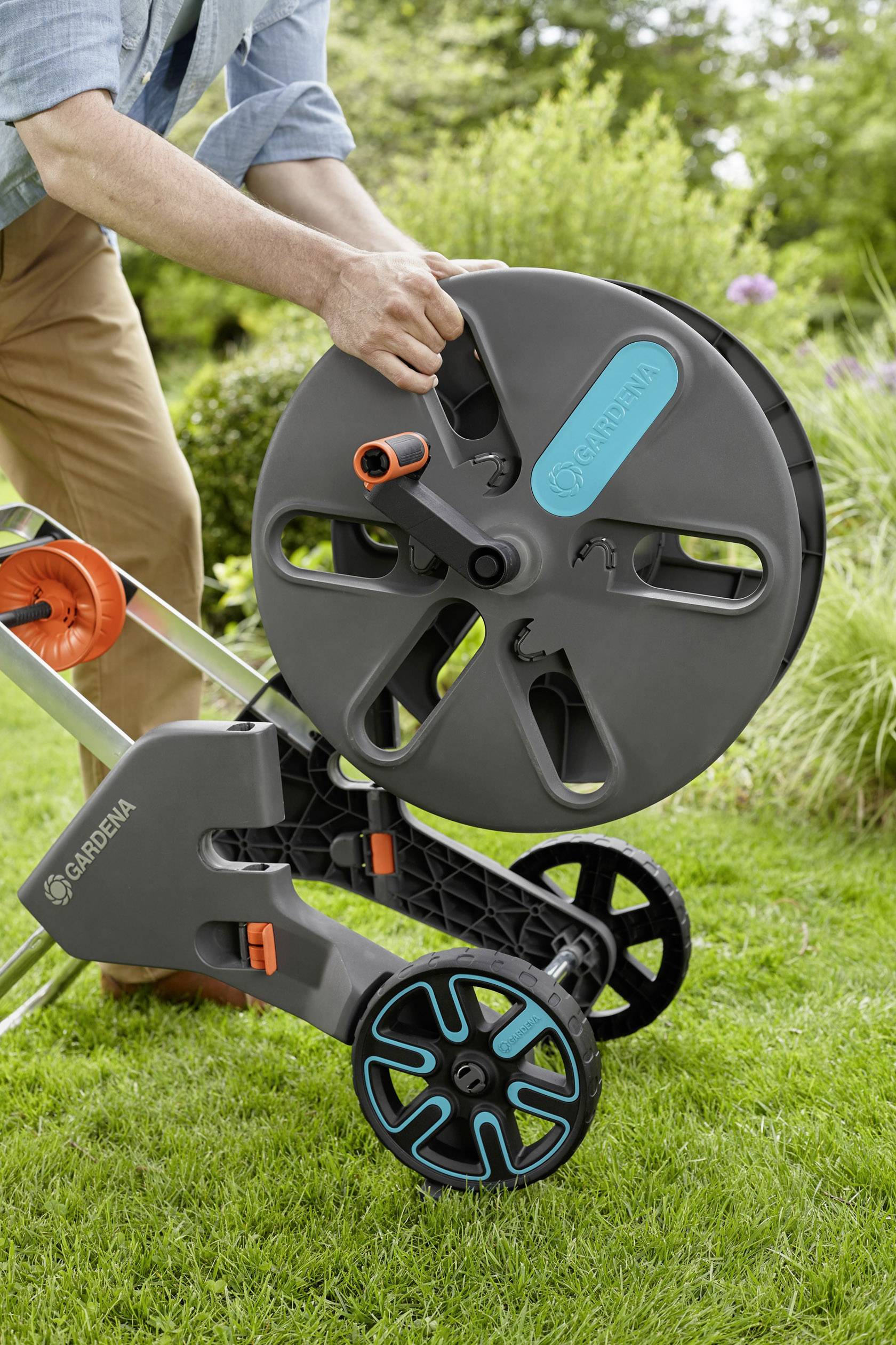 Person klemmt einen Gartenschlauch an eine mobile Schlauchtrommel. Im Hintergrund ist ein Garten zu sehen.