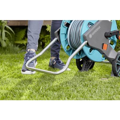 Eine Person benutzt eine Gartenschlauchrolle auf einem Rasen. Die Person trägt sportliche Kleidung und bewegt den Schlauchwagen.