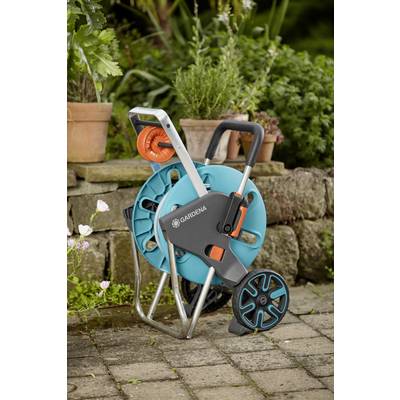 Gartenschlauchwagen mit Griff, orangem Anschluss und Aufrollmechanismus steht auf einer Terrasse vor einer Steinwand und Pflanzen.