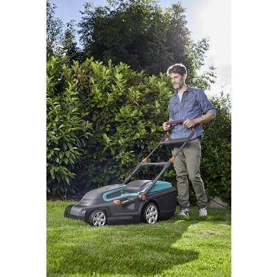 Eine Person mäht den Rasen mit einem Rasenmäher im Garten. Im Hintergrund sind grüne Büsche und Bäume unter blauem Himmel zu sehen.