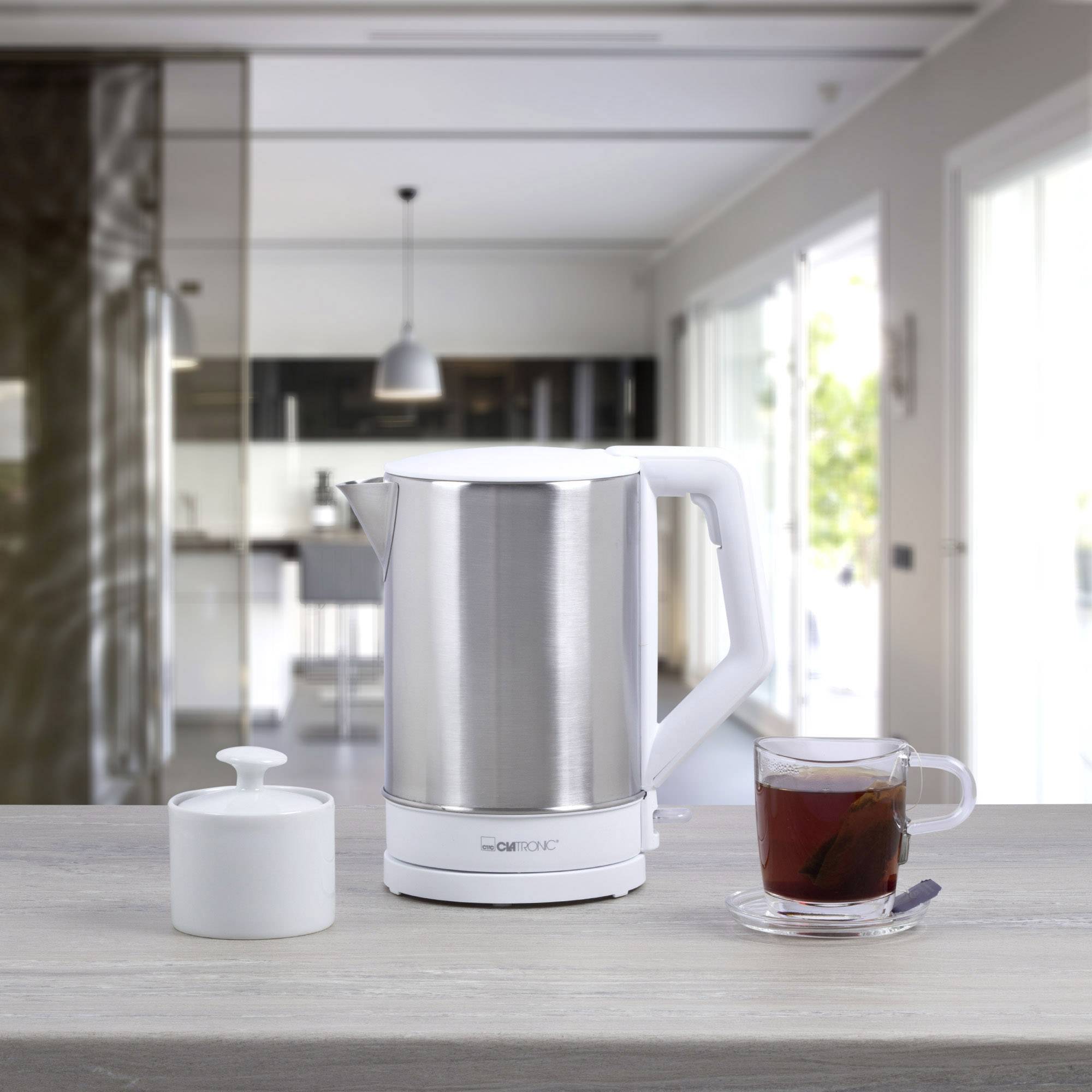 Ein elektrischer Wasserkocher aus Edelstahl steht auf einer Arbeitsplatte in einer modernen Küche, neben einer Tasse Tee und einer Zuckerdose.
