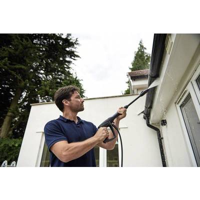 Ein Mann reinigt mit einem Hochdruckreiniger die Dachrinne eines Hauses. Im Hintergrund sind Bäume zu sehen.