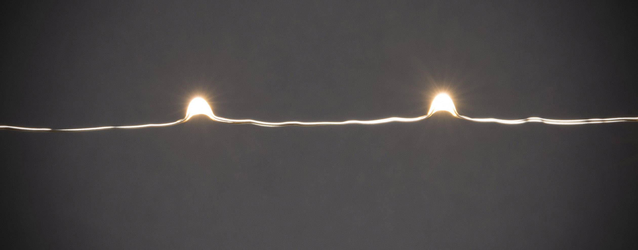 Zwei kleine Lichtpunkte auf einem dunklen Hintergrund, verbunden durch eine dünne Linie, erinnern an eine schlichte Lichterkette.
