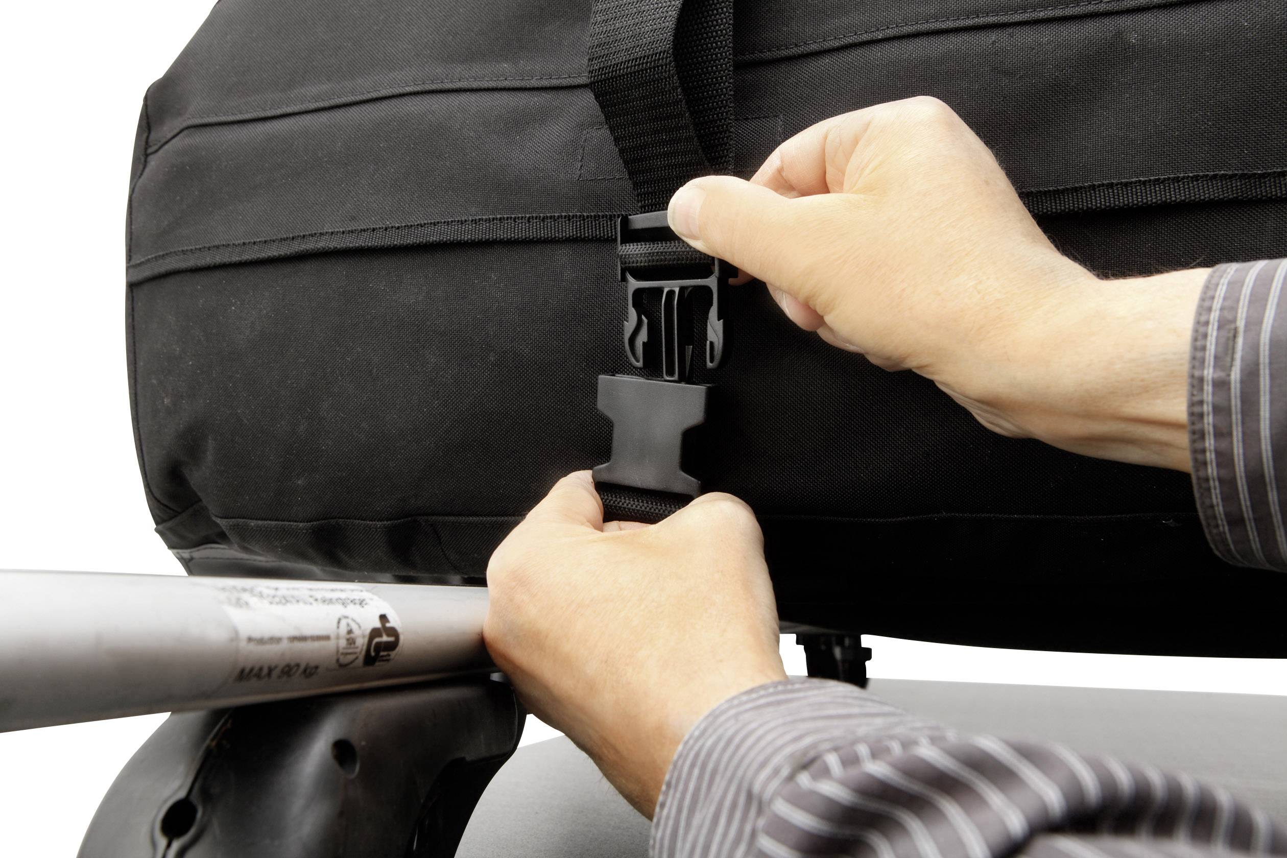 Zwei Hände befestigen einen schwarzen Gepäckriemen an einem Autodachträger. Sicherheitsmechanismus wird geschlossen.